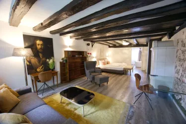 Ein gemütliches Zimmer mit Holzbalkendecke und moderner Einrichtung. Die Einrichtung umfasst ein Sofa, einen Tisch und einen bequemen Sessel.