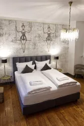 Ein modernes Schlafzimmer mit einem Doppelbett und eleganten Kissen. Die Wände sind mit einzigartigen Kunstwerken verziert, und eine stilvolle Deckenleuchte sorgt für eine gemütliche Atmosphäre.