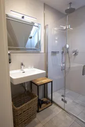 Ein modernes Badezimmer mit einer Dusche aus Glas und einem Waschbecken. Neben dem Waschbecken steht ein stilvoller Holztisch und ein Korb.