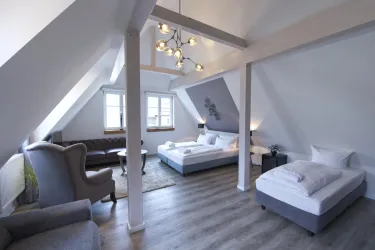 Ein modern gestaltetes Zimmer mit zwei Betten und gemütlichen Sitzgelegenheiten. Große Fenster sorgen für viel Tageslicht und eine helle Atmosphäre.