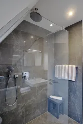 Eine moderne Dusche mit Glaswänden und elegantem Steinboden. Handtücher hängen an der Wand, und eine Regenbrause ist installiert.