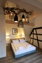 Ein modernes Schlafzimmer mit einem großen Bett und stilvollen Beleuchtungselementen. Die Wände sind hell gestrichen und es gibt eine rustikale Holzstruktur im Raum.