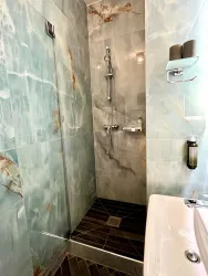 Eine moderne Dusche mit grauen Marmorfliesen und einer verglasten Duschabtrennung. Das Bad ist gut beleuchtet und hat eine elegante Ausstattung.