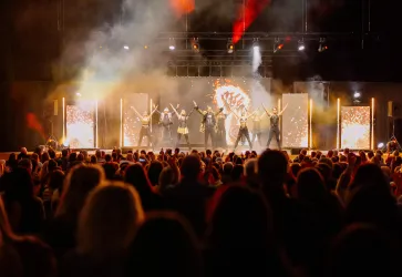Eine beeindruckende Live-Show mit Tänzern auf der Bühne vor einem begeisterten Publikum. Die Bühne ist mit bunten Lichtern und Effekten gestaltet.