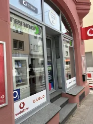 Ein Geschäft mit Schaufenstern, das Elektronik und Mobilfunkdienstleistungen anbietet. Sichtbar sind Logos von Vodafone, o2 und o.tel.o.