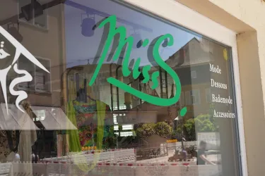 Ein Schaufenster mit dem Schriftzug „Miss“ in grüner Schrift. Darunter stehen die Kategorien Mode, Dessous, Bademode und Accessoires.