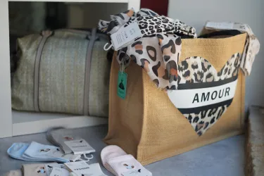 Eine stilvolle Tasche mit einem Herzmotiv und dem Schriftzug "AMOUR". Daneben liegen verschiedene Socken und ein weiterer Beutel.