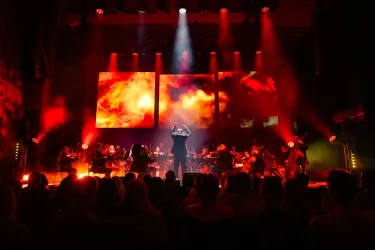 Ein spannendes Konzert mit einer Band auf der Bühne. Der Hintergrund zeigt farbenfrohe Lichteffekte und große Bildschirme.