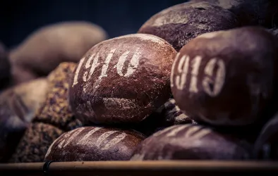 Eine Ansammlung von braunen Broten mit der Jahreszahl 1910 auf der Oberfläche. Die Brote sind unregelmäßig geformt und wirken frisch gebacken.