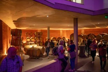 Ein moderner Weinkeller mit Holzfässern und sanfter Beleuchtung. Besucher stehen zusammen und genießen die Atmosphäre.