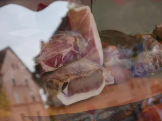 Eine Auswahl an Fleischstücken in einer Auslage. Die Präsentation zeigt verschiedene Schinken und Wurstwaren.