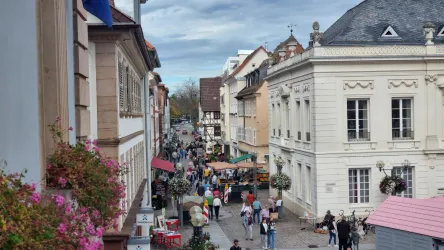 Eine belebte Straße mit historischen Gebäuden und bunten Ständen. Menschen schlendern umher und genießen die Atmosphäre.