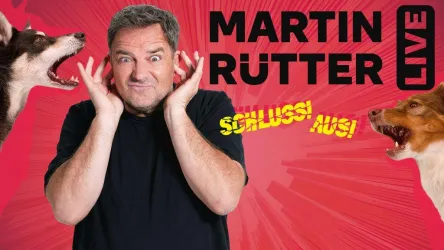 Ein Mann hält sich die Ohren zu und sieht überrascht aus. Im Hintergrund sind zwei bellende Hunde und der Titel "Martin Rütter Live" zu sehen.