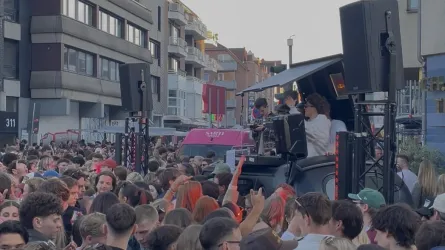 Eine große Menschenmenge feiert auf einer Straße, während DJs Musik spielen. Die Atmosphäre ist lebhaft und energiegeladen.