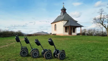 Eine kleine Kirche steht auf einer Wiese mit Blick auf die Umgebung. Vor der Kirche sind mehrere Segways aufgestellt.