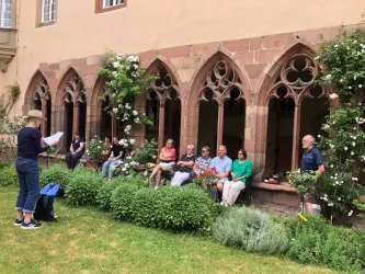 Eine Gruppe von Menschen sitzt in einem Innenhof mit historischen Bögen. Einige hört aufmerksam zu, während eine Person vor ihnen spricht.