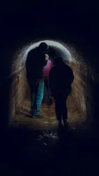 Eine dunkle Tunnelpassage mit mehreren Personen, die sich darin bewegen. Der Tunnel hat eine kurvenförmige Decke und ist schwach beleuchtet.