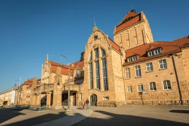 Ein historisches Gebäude mit einer beeindruckenden Architektur und vielen Fenstern. Die Sonne scheint auf die Fassade und zeigt die Details der Steinstruktur.