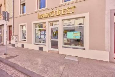 Ein modernes Geschäft mit großen Fenstern und einer goldenen Beschriftung. Die Fassade ist schlicht und hell gestaltet.