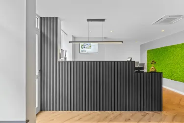 Ein moderner Empfangsbereich mit einer schwarzen Theke und einem grünen Wandarrangement aus Pflanzen. Der Raum hat helle Wände und einen eleganten Holzfußboden.