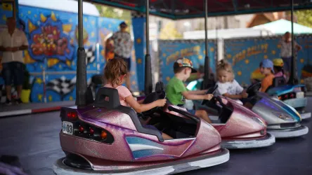 Kinder fahren mit Autoscootern in einem Vergnügungspark. Im Hintergrund sind bunte Dekorationen zu sehen.