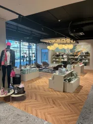 Ein stilvolles Modegeschäft mit modernen Regalen und einer einladenden Atmosphäre. Verschiedene Taschen und Kleidung sind auf Verkaufstischen präsentiert.