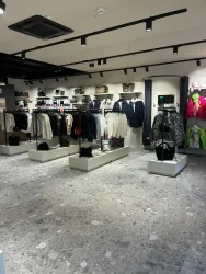 Ein moderner Bekleidungsladen mit verschiedenen Kleidungsstücken an offenen Regalen. Der Boden ist aus grauem Material und die Beleuchtung sorgt für eine helle Atmosphäre.