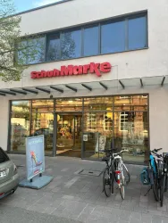 Ein Geschäft mit der Beschriftung "SchonMarke" an der Vorderseite. Es stehen Fahrräder vor dem Eingang und es gibt ein Werbeschild.