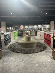 Ein modernes Geschäft mit Regalen voller Produkte in verschiedenen Farben. In der Mitte steht ein runder Sitzbereich auf einem grauen Teppich.