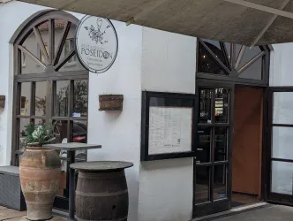 Das Bild zeigt den Eingang eines Restaurants mit dem Namen "Poseidon". Es hat große Fenster und eine einladende Atmosphäre.