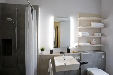 Ein modernes Badezimmer mit einer begehbaren Dusche und einem schlichten Waschbecken. Helle Wände und eine gut organisierte Ablage schaffen eine einladende Atmosphäre.