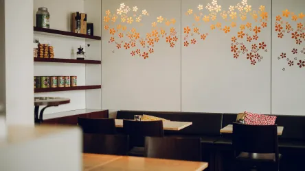 Ein modernes Café mit einem gemütlichen Innenraum. Die Wände sind mit dekorativen Blumenmotiven und Regalen mit einem Sortiment an Produkten geschmückt.