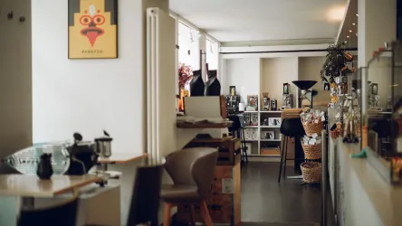 Ein modernes Café mit einer einladenden Atmosphäre. Es gibt Tische, Stühle und dekorative Elemente an den Wänden.