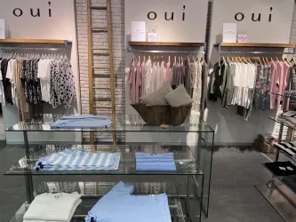 Ein Modestore mit verschiedenen Kleidungsstücken auf den Regalen. Im Vordergrund liegt eine Glasvitrine mit mehreren T-Shirts.