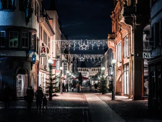 Eine festlich beleuchtete Straße bei Nacht mit Weihnachtslichtern und dekorierten Tannenbäumen. Die Atmosphäre ist gemütlich und einladend.