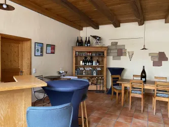 Ein gemütlicher Raum mit Holzdecken und Fliesenboden. Regal mit Weinflaschen und Sitzgelegenheiten.