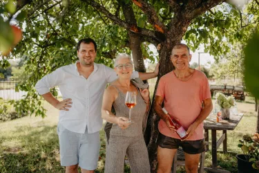 Drei Personen stehen unter einem Baum und lächeln. Sie halten Getränke in der Hand und wirken entspannt.