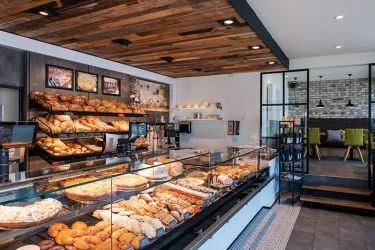 Eine moderne Bäckerei mit einer Vielzahl von frischen Brötchen und Gebäcken in der Vitrine. Im Hintergrund sind gemütliche Sitzgelegenheiten und ein helles, einladendes Ambiente zu sehen.