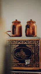 Zwei kupferne Kaffeekannen stehen auf einer kunstvoll verzierten Box. Die Kannen haben einen klassischen, traditionellen Stil.