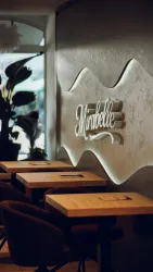 Ein modernes Café mit Holztischen und stilvollen Stühlen. An der Wand sieht man das Logo „Mirabelle“ in ansprechendem Design.