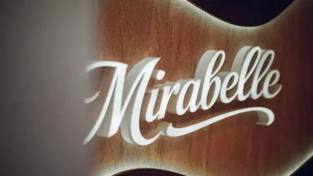 Ein Detail eines Gitarrenkorpus mit dem Schriftzug "Mirabelle". Die Holzoberfläche hat einen warmen, natürlichen Farbton.