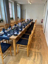 Ein eleganter Veranstaltungstisch mit Holzoberfläche und blauen Tischdecken. Der Tisch ist festlich gedeckt für eine Zusammenkunft mit Blumen und Glaswaren.