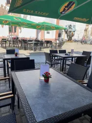 Ein gemütlicher Außenbereich mit Tisch und Stühlen unter grünen Sonnenschirmen. Im Hintergrund sind weitere Tische in einer einladenden Atmosphäre zu sehen.