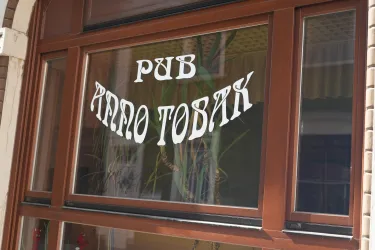 Ein Fenster mit der Aufschrift "Pub Anno Tobak". Die Schrift ist auffällig und befindet sich in einem Holzrahmen.