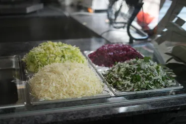 Frische Zutaten für Salate auf einem Tisch. Es sind gehackter Weißkohl, rote Beete und Kräuter sichtbar.