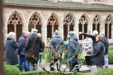 Eine Gruppe von Menschen steht in einem Innenhof eines Klosters. Sie scheinen einer Führung zu folgen und diskutieren miteinander.