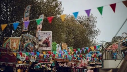 Ein lebhaftes Jahrmarkt mit bunten Fahnen und zahlreichen Ständen. Die Atmosphäre ist festlich und einladend.