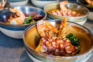 Eine Schüssel mit Garnelen und Oktopus, umgeben von frischem Gemüse. Die Farben der Speisen sind lebhaft und appetitlich.