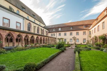 Ein schöner Innenhof mit gepflegtem Rasen und hübschen Hecken. Umgeben von historischen Gebäuden und einem klaren Himmel.