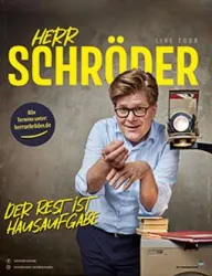 Ein fröhlicher Mann mit Brille steht an einem Tisch und hält eine alte Filmkamera. Der Text kündigt seine Live-Tour mit dem Titel "Der Rest ist Hausaufgabe" an.